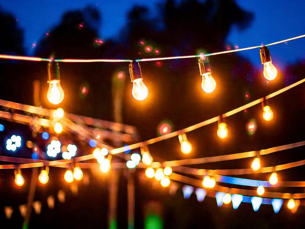 Warm Edison-bulb string lights crisscrossing outdoors against a twilight sky
