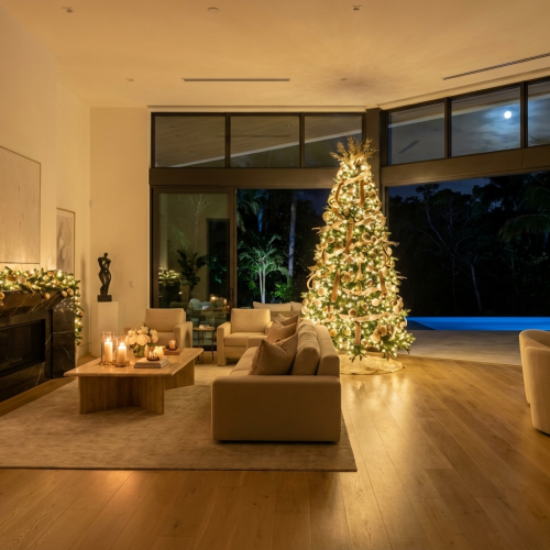 Modern South Florida living room decorated for the holidays with a gold Christmas tree and pool view at night
